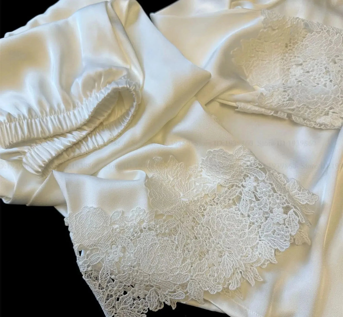 Close-up of white satin fabric with lace detailing on a black background